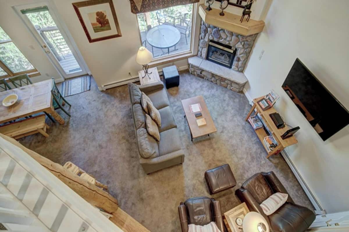 A spacious living area with a stone fireplace, a sofa, a coffee table, and a TV mounted on the wall.