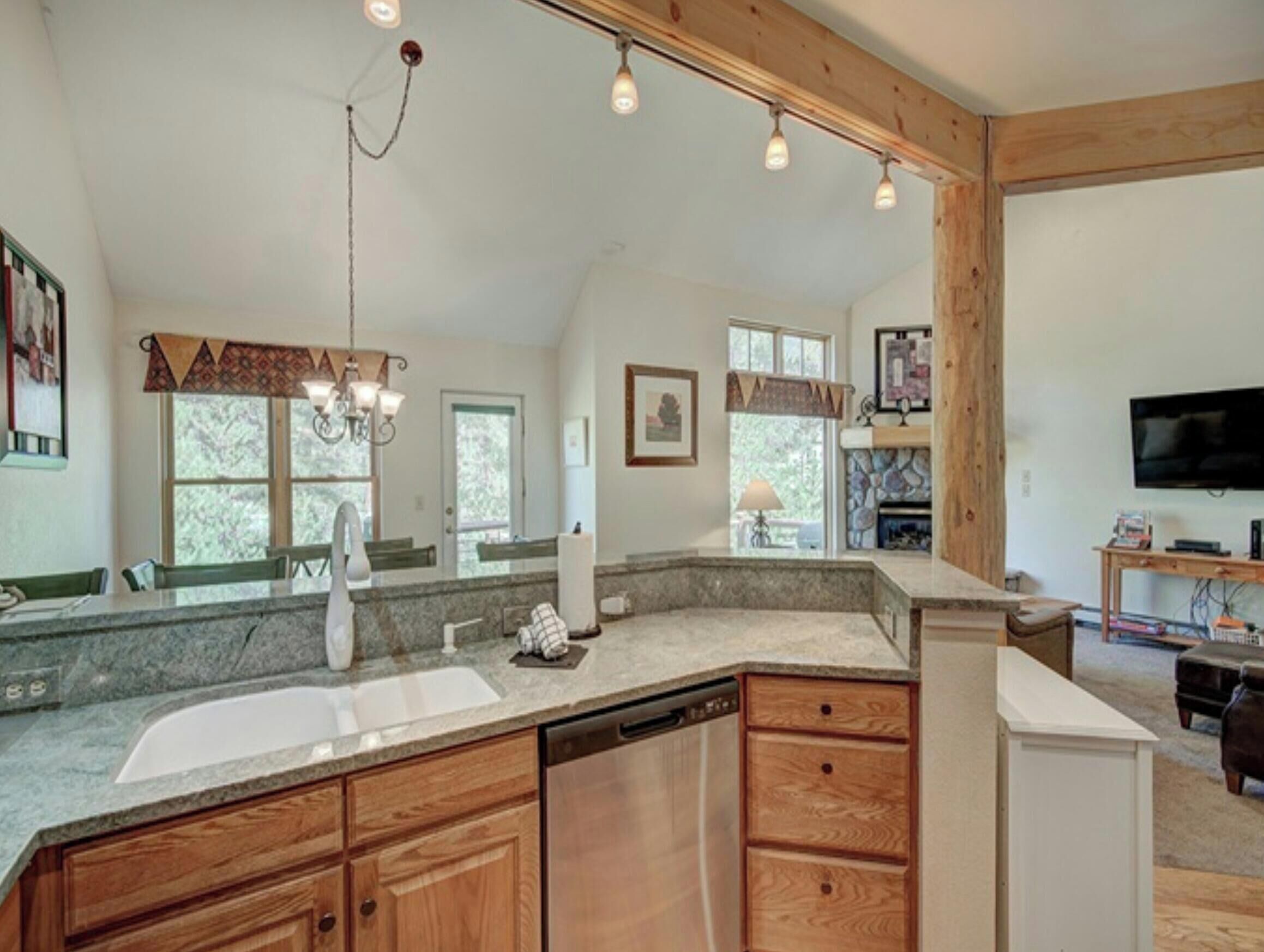 A kitchen with a granite countertop, wooden cabinets, a dishwasher, and a stone fireplace.