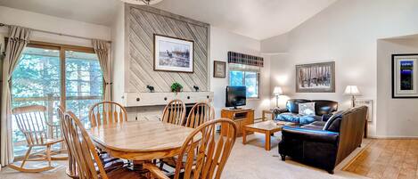 A spacious living room with a wooden dining table, comfortable seating, a television, and a fireplace.