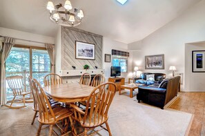 A spacious living room with a wooden dining table, comfortable seating, a television, and a fireplace.