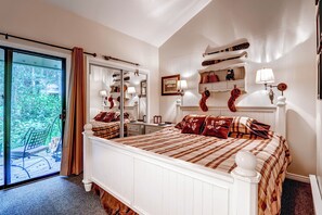 A bedroom with a large bed, a sliding glass door to a deck, and a mirror above the bed.