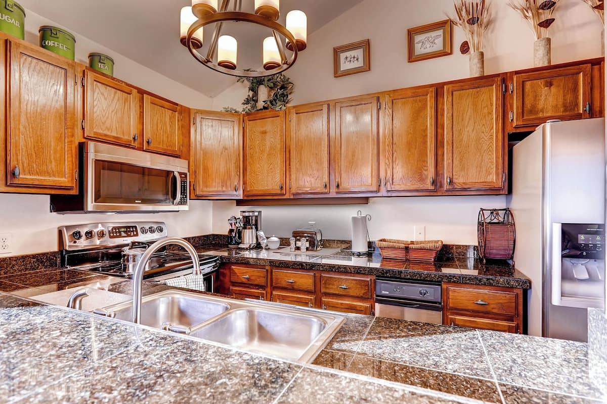A kitchen with wooden cabinets, granite countertops, stainless steel appliances, and a chandelier.