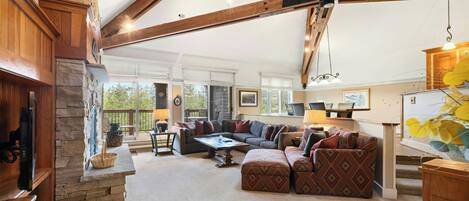 A spacious living room with a stone fireplace, wooden beams, and a large sectional sofa.