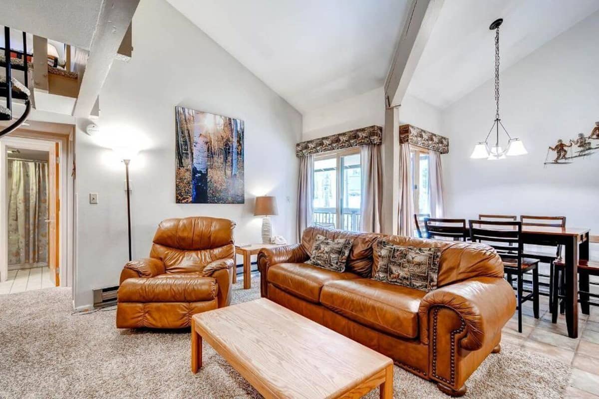 A spacious living room with a brown leather sofa, a wooden coffee table, and a dining area with a table and chairs.