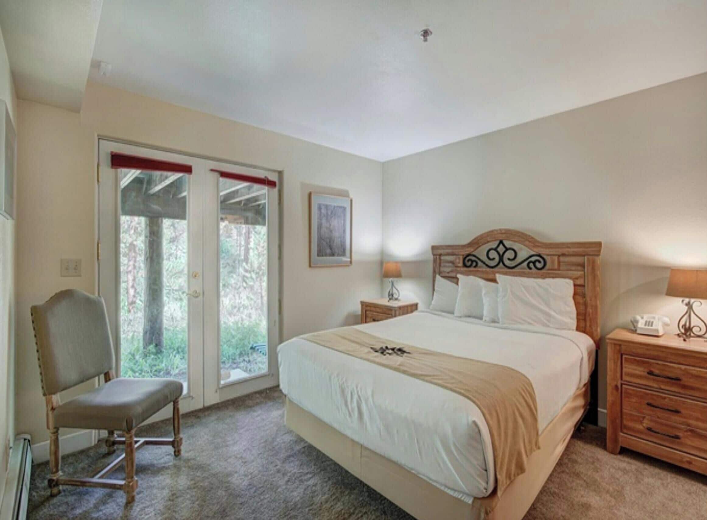 A bedroom with a bed, a chair, a nightstand, a lamp, and a door leading to a balcony.