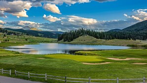 A golf course with a lake, surrounded by mountains and a wooden fence. - Forest Condominiums by Vail Resorts (Keystone)