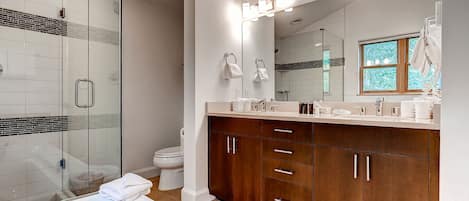 A modern bathroom with a glass shower enclosure, a large mirror with lights, wooden cabinets, and a bathtub.