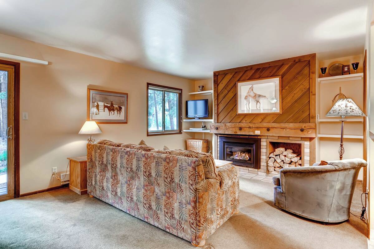 A cozy living room with a fireplace, a sofa, a television, and a fireplace mantel with framed pictures.