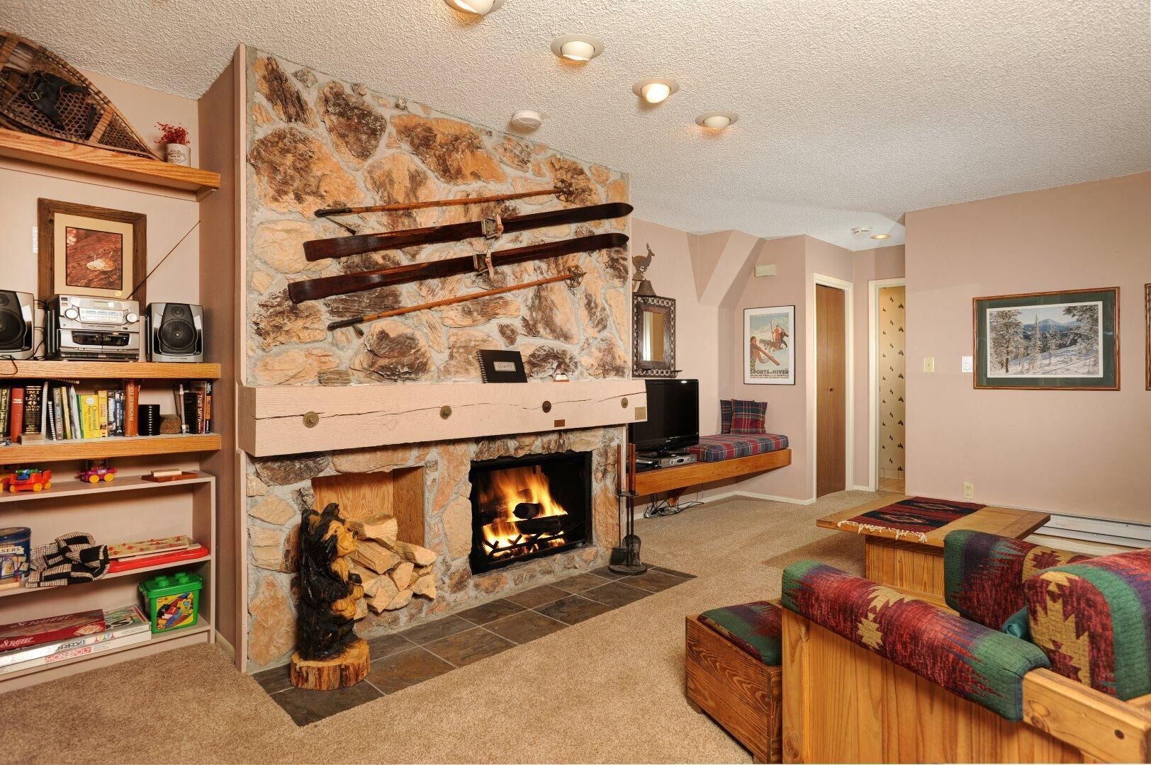 A cozy living room with a stone fireplace, a bookshelf, a television, and a colorful sofa.