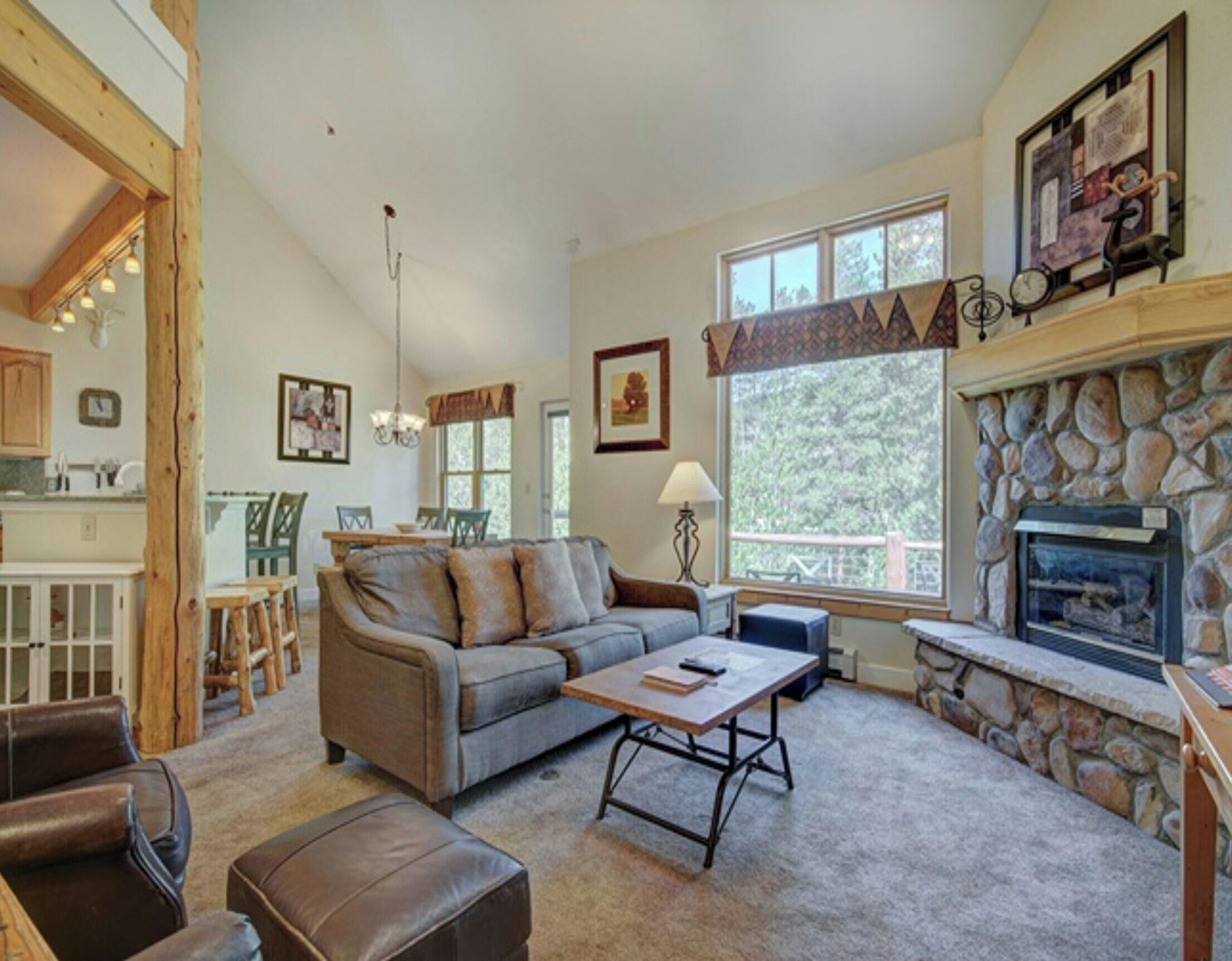 A cozy living room with a stone fireplace, a sofa, a coffee table, and a dining area with chairs.