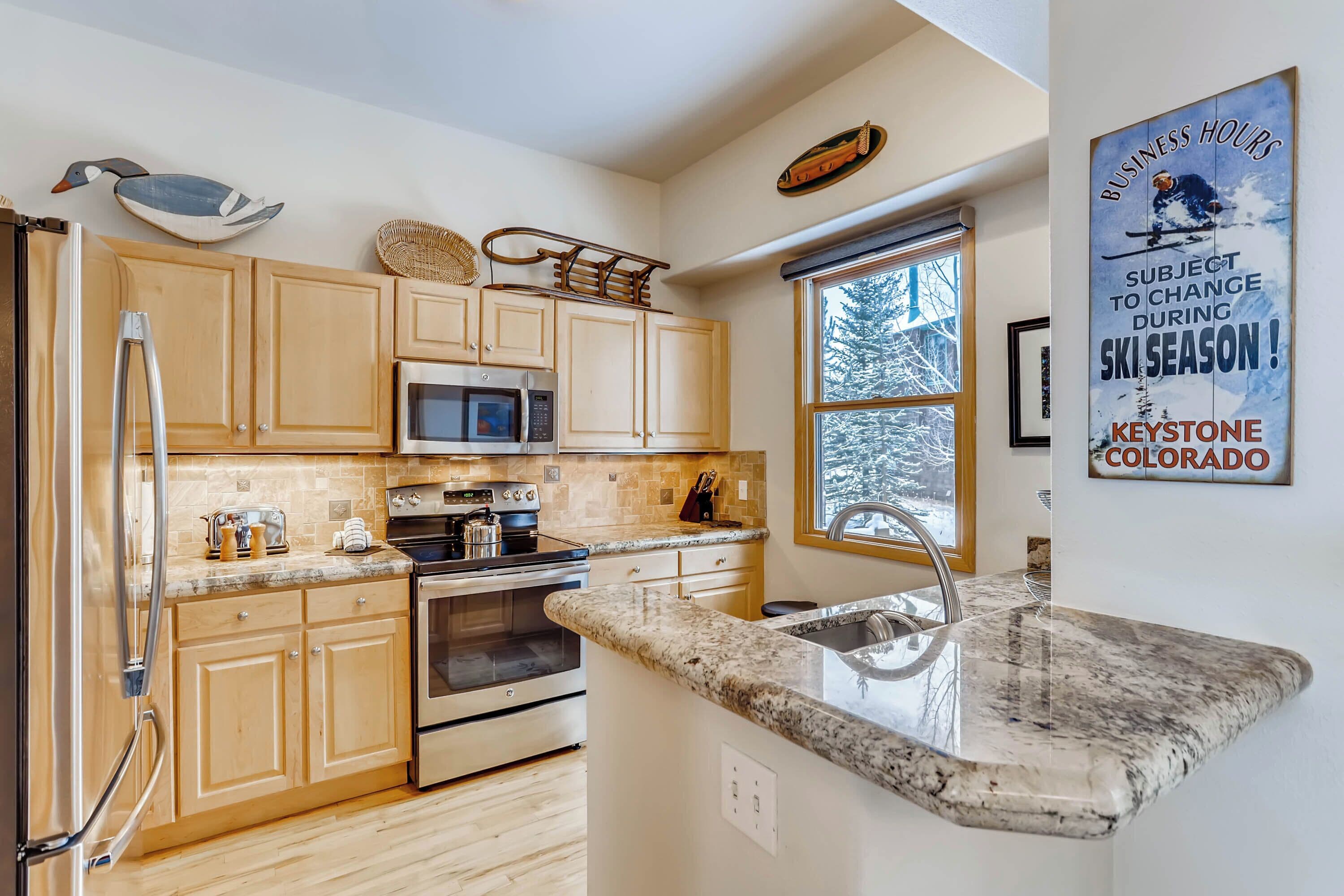 A modern kitchen with wooden cabinets, a stainless steel refrigerator, a microwave, an oven, and a granite countertop.