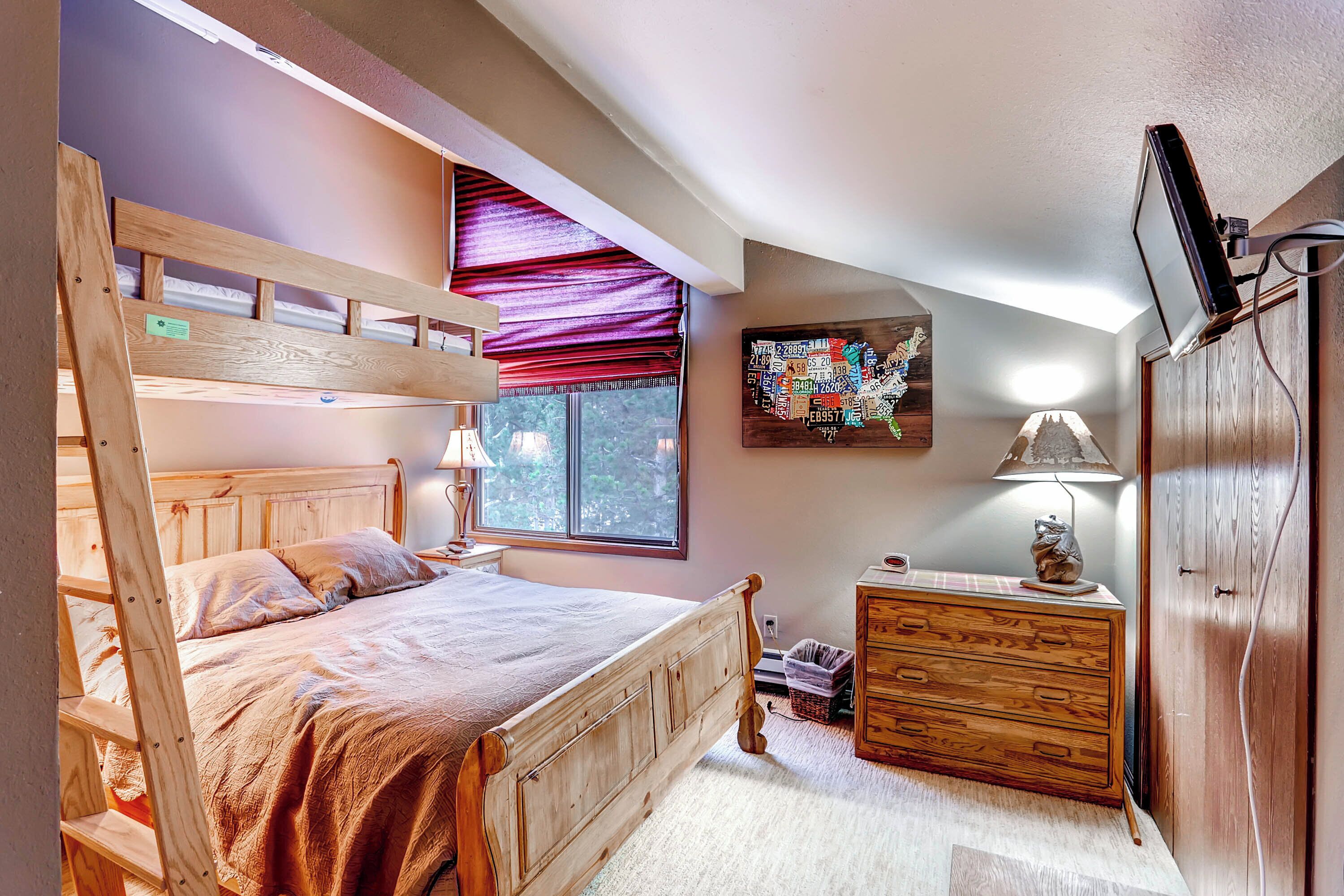 A bedroom with a bunk bed, a dresser, a lamp, a map on the wall, and a TV mounted on the wall.