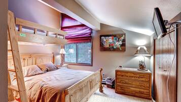 A bedroom with a bunk bed, a dresser, a lamp, a map on the wall, and a TV mounted on the wall.