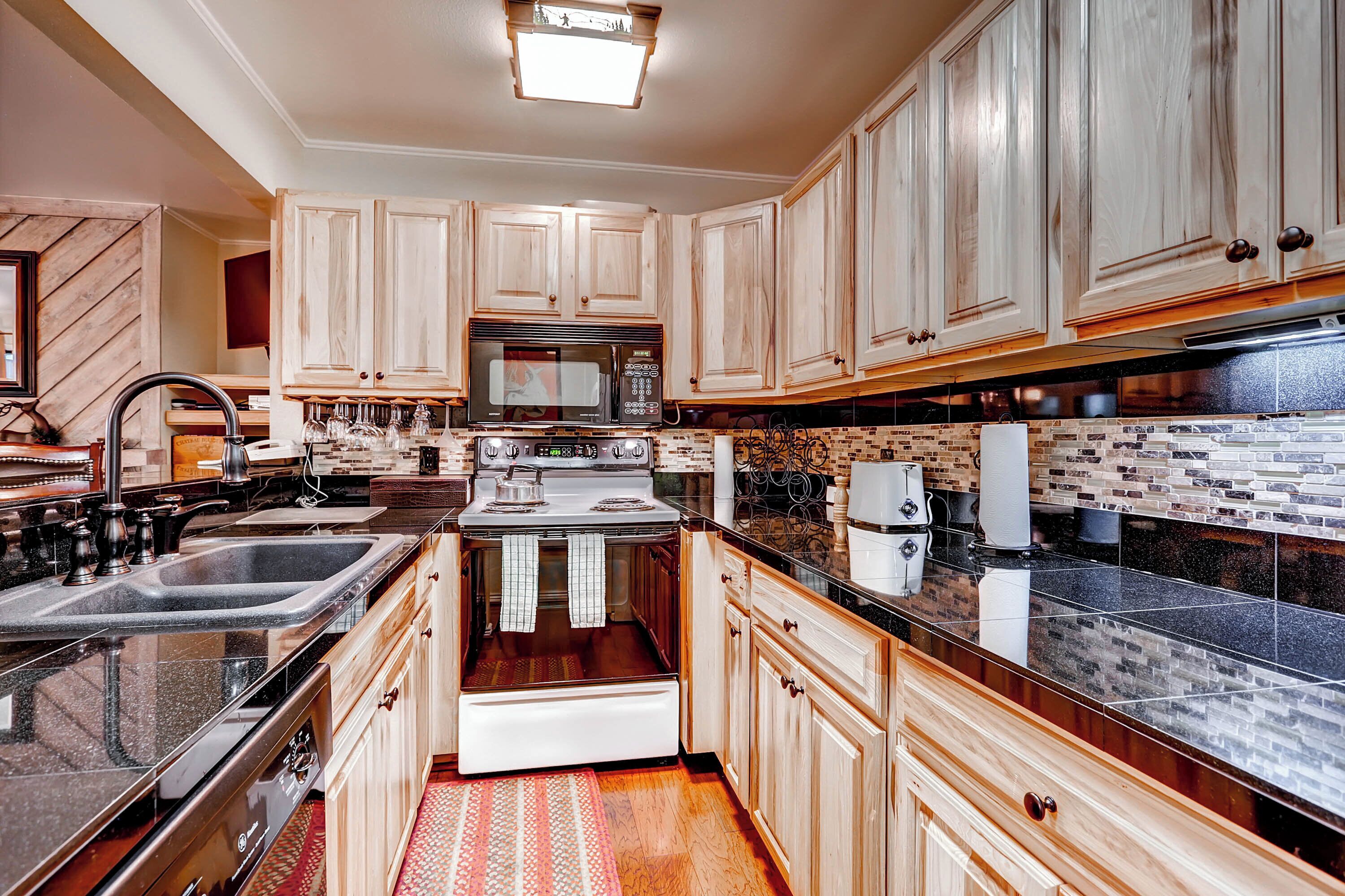 A kitchen with wooden cabinets, a microwave, stove, sink, and a patterned backsplash.