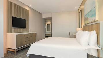 Habitación de hotel con una cama grande, un televisor de pantalla plana montado en un panel de madera, un escritorio con una silla y un cuadro en la pared.