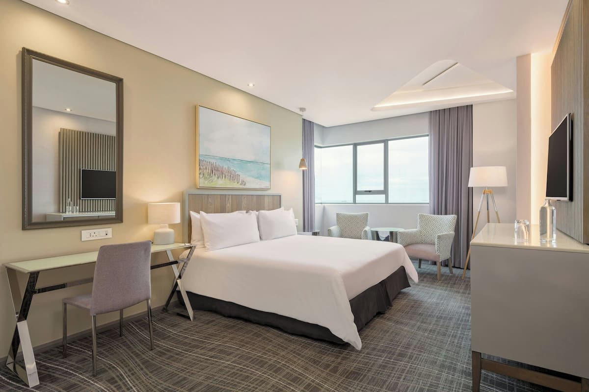 Une chambre d’hôtel équipée d’un lit, d’un bureau, d’une chaise, d’une télévision et d’une grande fenêtre.