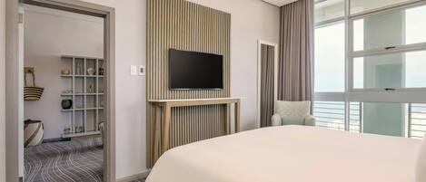 A hotel room with a large bed, a television mounted on a wooden panel, a window with curtains, and a patterned carpet.