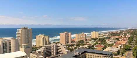 Paisagem costeira com edifícios altos, uma praia e céu azul límpido.