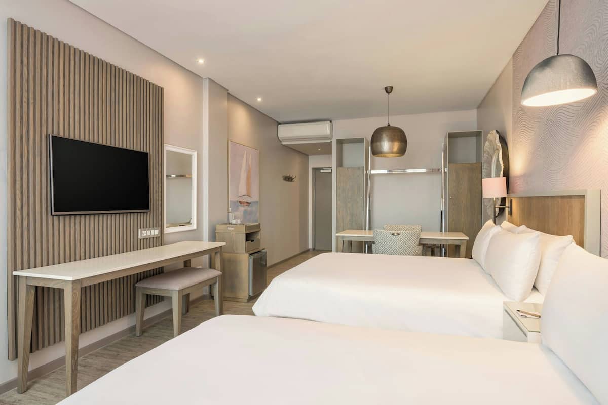 Une chambre d’hôtel moderne équipée d’un téléviseur à écran plat, de deux lits, d’un bureau et d’un grand miroir.