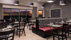 A restaurant with multiple tables, chairs, and a large window offering a city view.