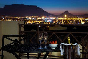 A table with two glasses, a bowl of strawberries, and a bottle of champagne on a balcony overlooking a cityscape at dusk. - Protea Hotel by Marriott Cape Town Tyger Valley (Cape Town)
