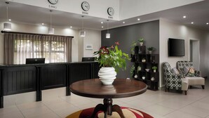 A reception area with a round table, a laptop, a potted plant, a television, and a seating area with a patterned chair.