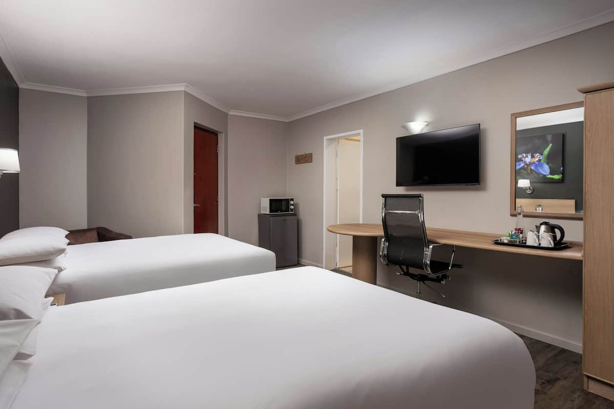 Ein Hotelzimmer mit zwei Betten, einem Schreibtisch mit Stuhl, einem Fernseher, einer Mikrowelle und einem kleinen Schrank.