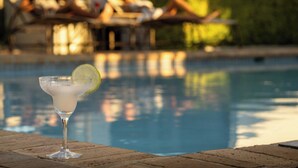 A clear view of a swimming pool with a glass of a beverage on a table.