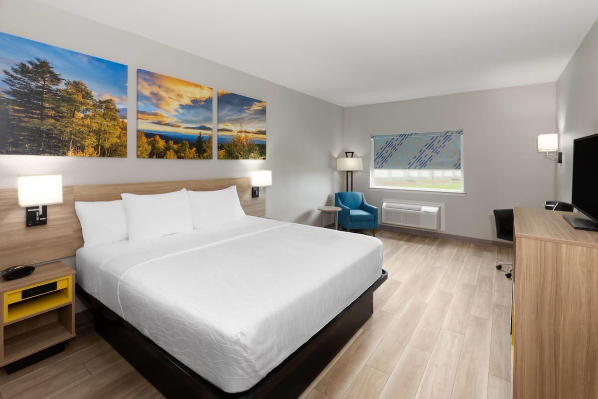 A hotel room with a large bed, two wall-mounted paintings, a desk with a computer, and a chair.