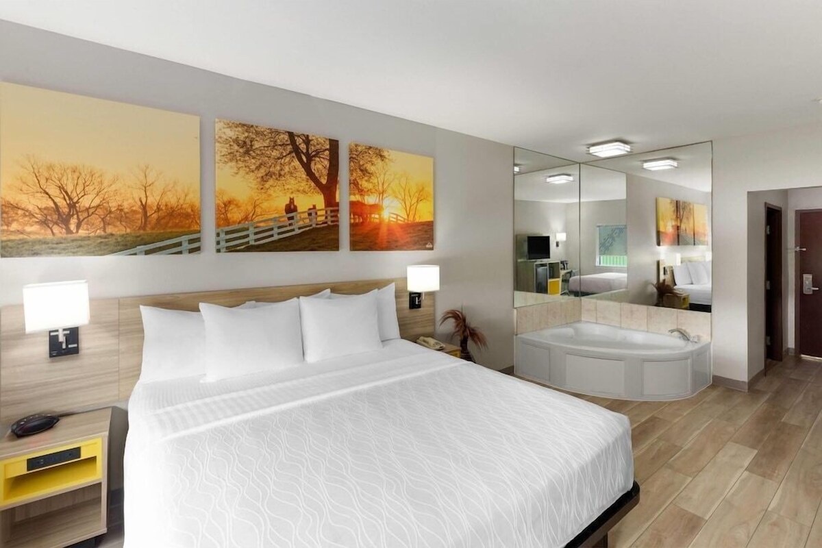 A hotel room with a large bed, a sitting area with a view, a large mirror, and a bathtub.