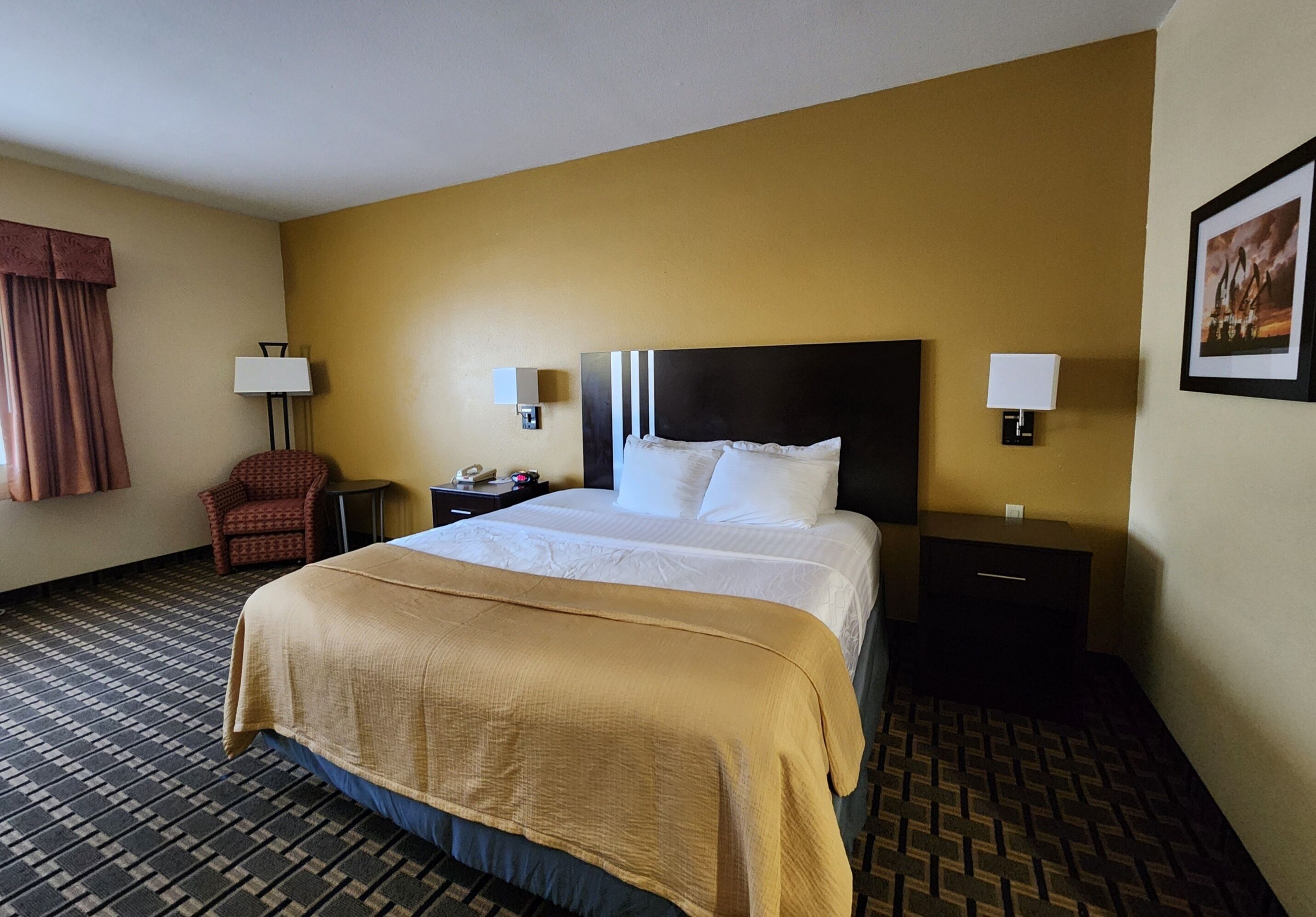 A hotel room with a large bed, two bedside tables, a chair, and a lamp.