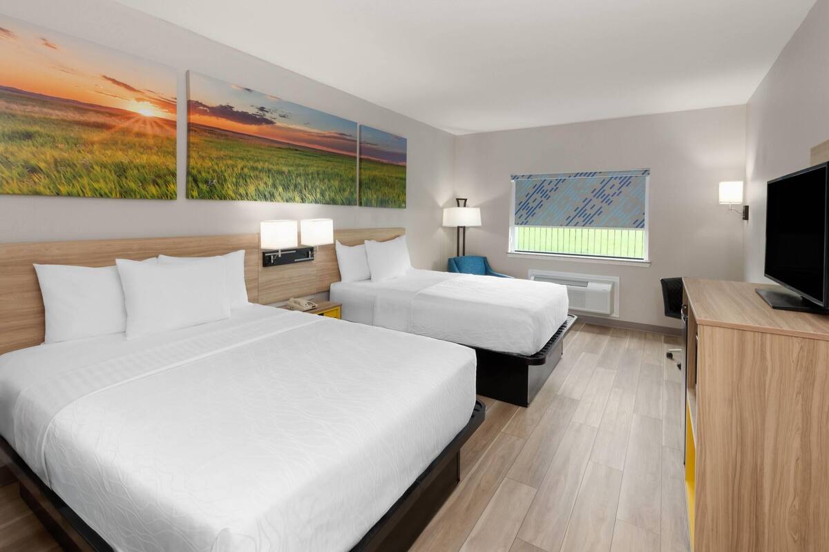 A hotel room with two beds, a desk, a TV, and artwork on the walls.