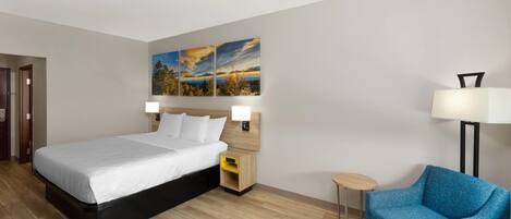 Una habitación de hotel con una cama grande, un sillón azul, una mesita de noche y una lámpara de pared.