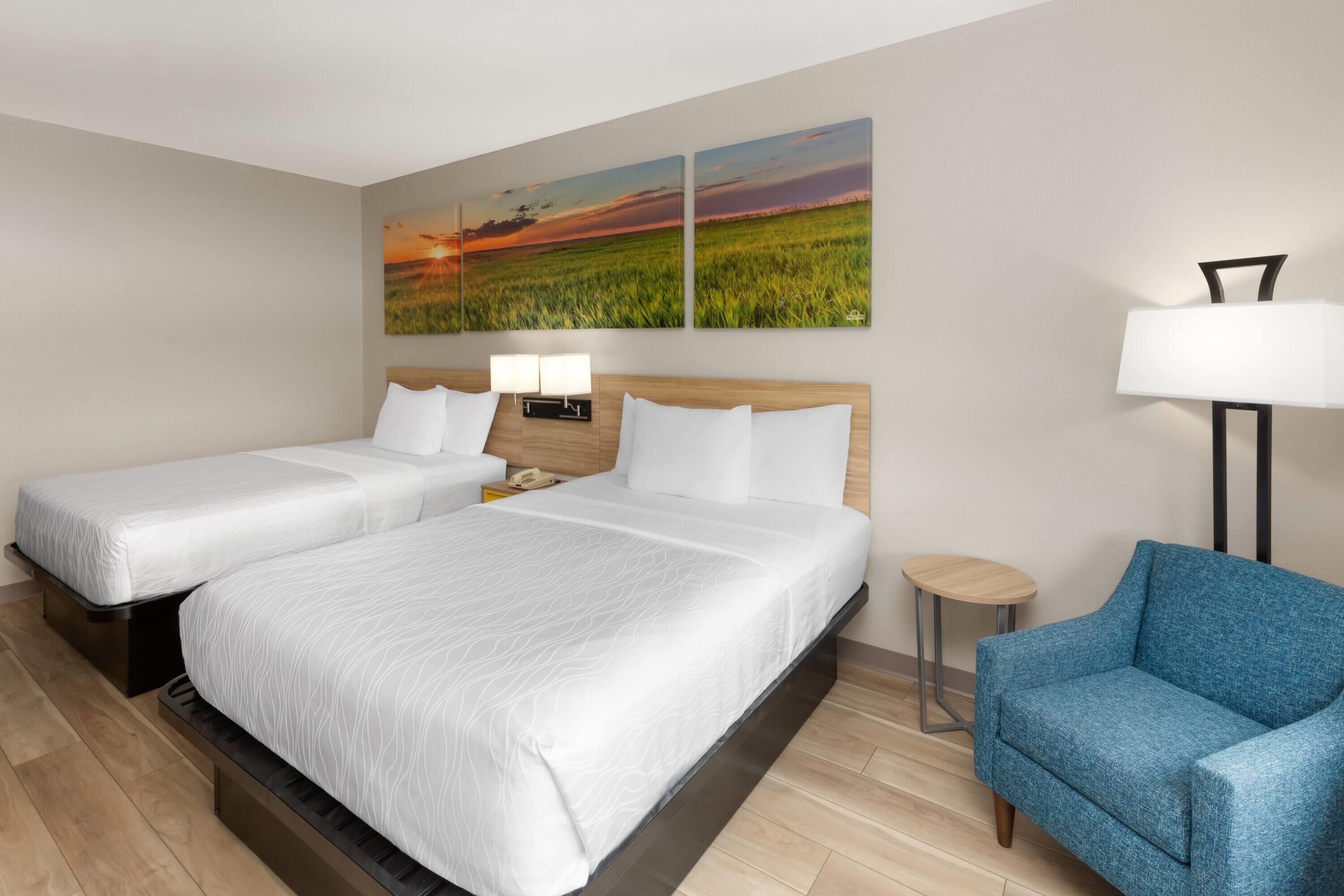 Een hotelkamer met twee bedden, een blauwe fauteuil, een klein rond tafeltje en twee wandlampen.