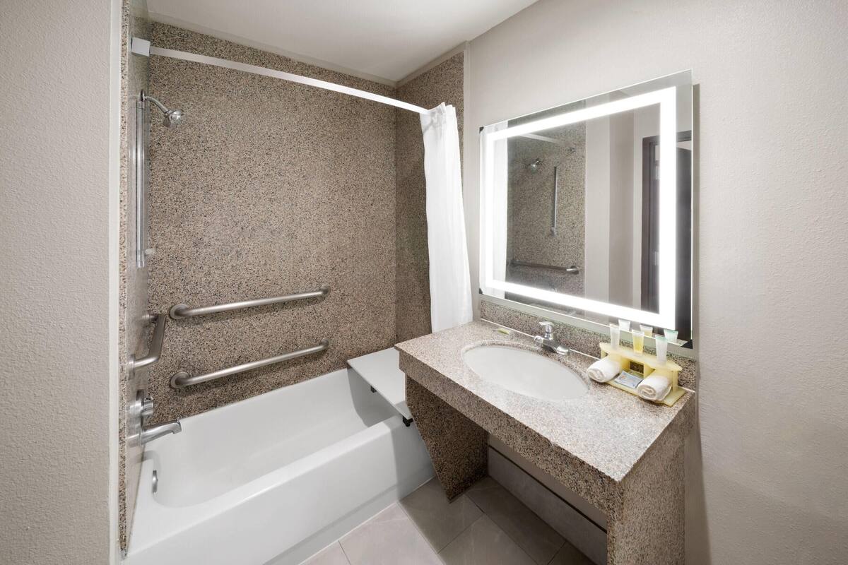 A bathroom with a bathtub, a sink with a mirror, and handrails.