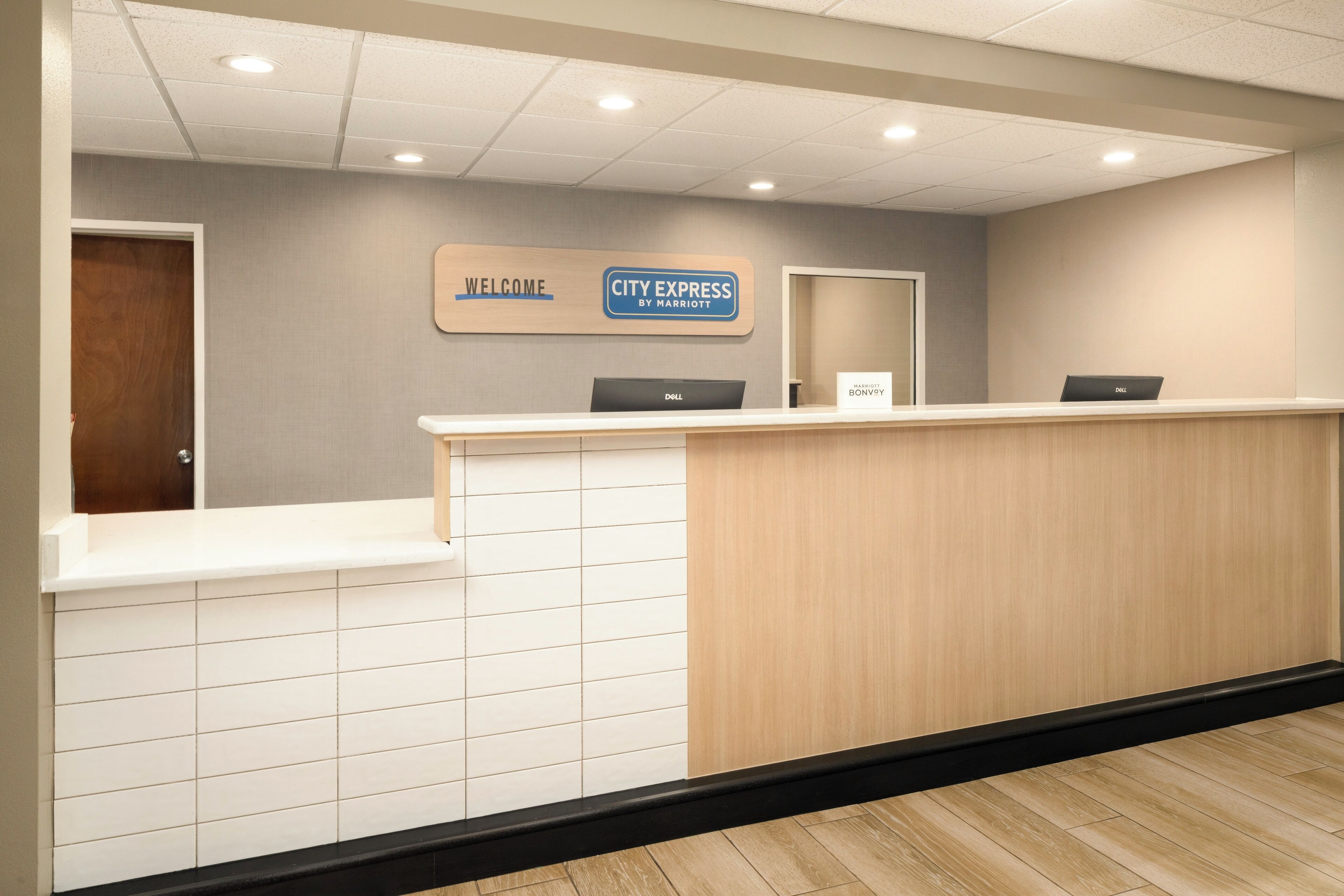A reception desk with a 'Welcome' sign and 'City Express by Marriott' sign, two laptops, and a wooden counter.
