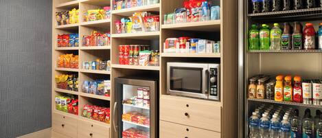 A kitchenette with shelves stocked with snacks, a microwave, and a refrigerator.