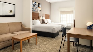 A hotel room with a sofa, two beds, a desk, and a chair.