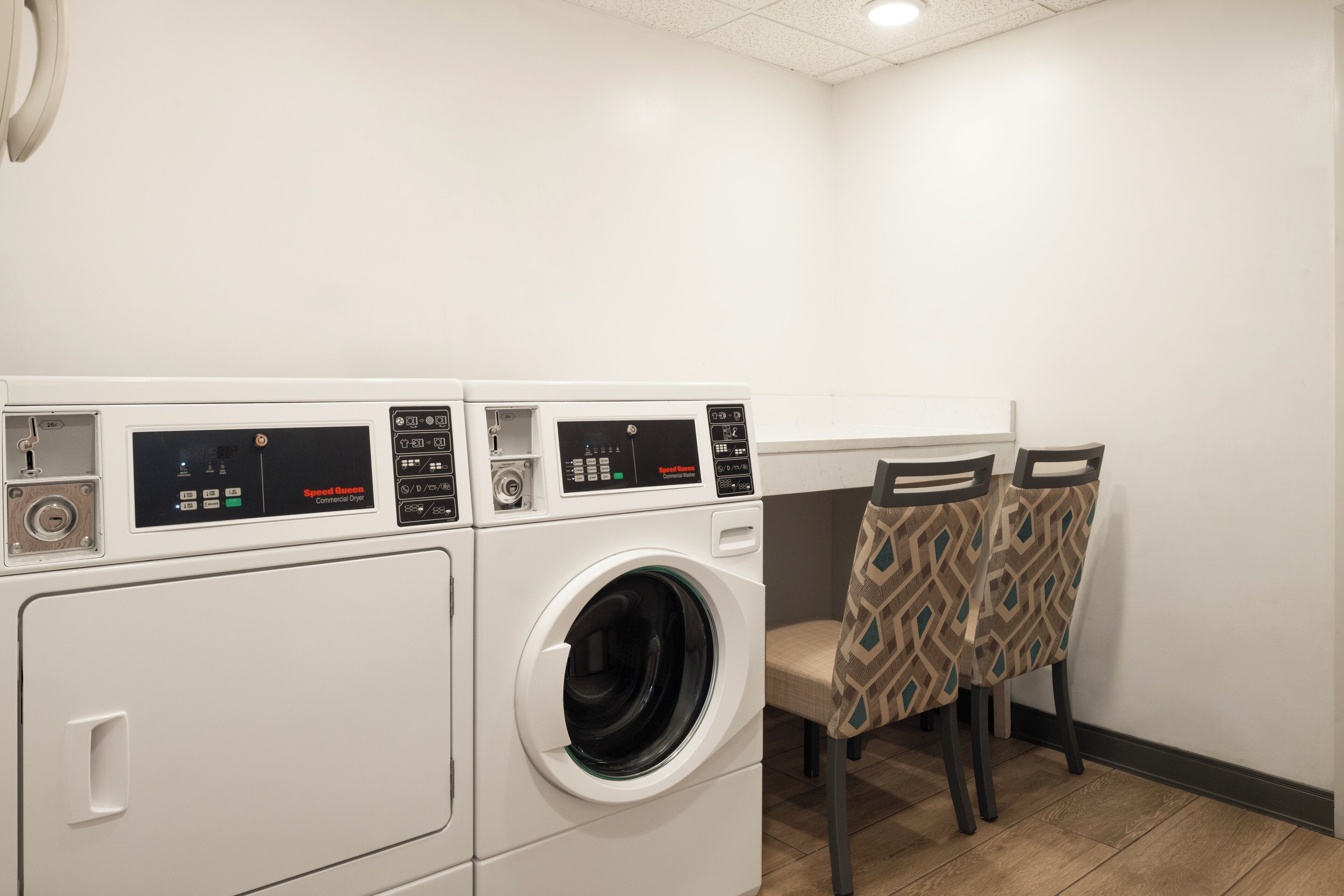 A laundry area with two front-loading washing machines and two chairs with patterned upholstery.