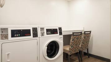A laundry area with two front-loading washing machines and two chairs with patterned upholstery.