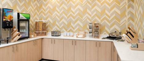 A modern kitchen with a herringbone patterned wall, a juice dispenser, a coffee machine, and various kitchen appliances.