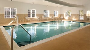 An indoor swimming pool with clear water, surrounded by white chairs and a slide.