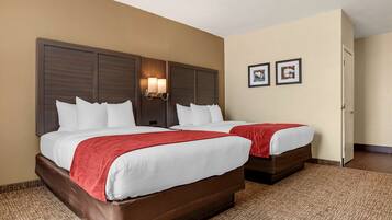 A hotel room with two beds, a large wooden headboard, a red throw blanket, and two framed pictures on the wall.