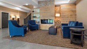 A modern living room with blue sofas, a coffee table, and a TV mounted on a wooden wall. There is a staircase with a railing and a door leading to another room. - Comfort Inn & Suites Millbrook - Prattville (Millbrook)
