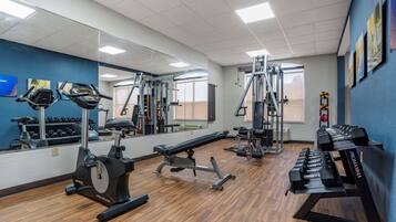 A gym with cardio machines, weightlifting equipment, and dumbbells.