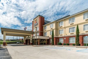 Un hotel Comfort Inn & Suites con área de estacionamiento techada, espacios de estacionamiento accesibles para personas con discapacidad y fachada de ladrillo.