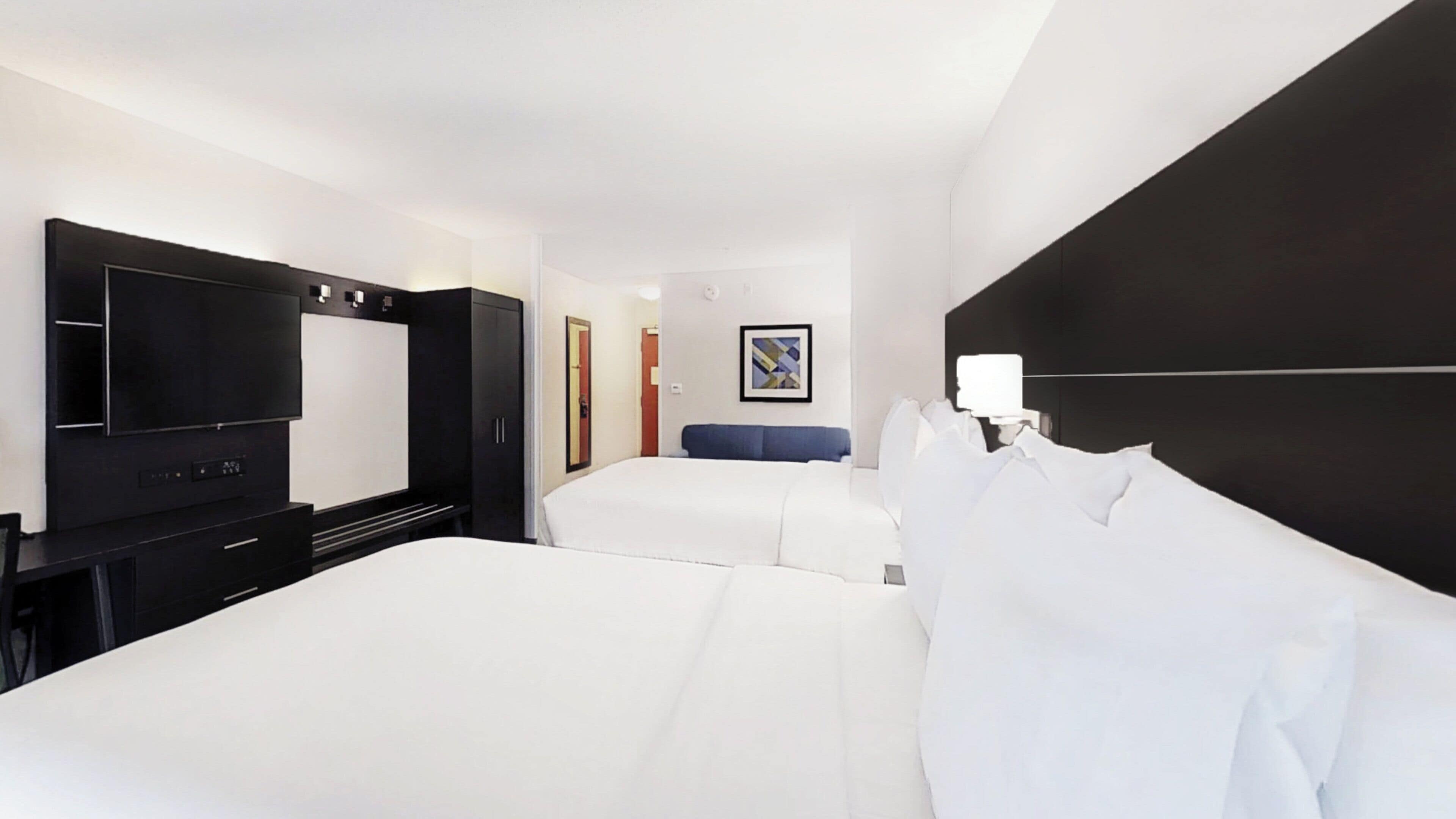 A hotel room with two beds, a TV, a desk, and a framed picture on the wall.
