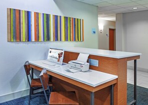 A reception desk with a laptop, printer, and chair in a modern office space with a colorful striped wall. - Holiday Inn Express New Orleans East by IHG (New Orleans)