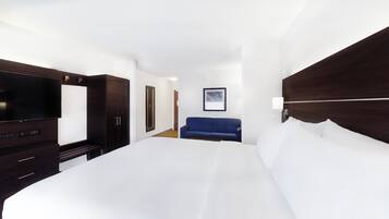 A hotel room with a large bed, a TV, a wardrobe, and a blue sofa.