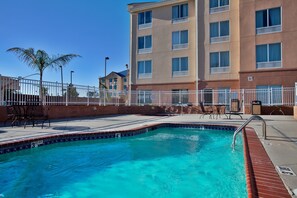 A swimming pool with a tiled edge, surrounded by a white fence, and a building with multiple windows in the background. - Holiday Inn Express New Orleans East by IHG (New Orleans)